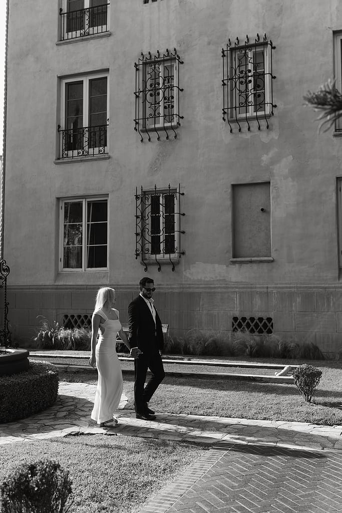 Capturing a candid moment as the engaged pair walks hand in hand through the hotel's well-kept courtyard.