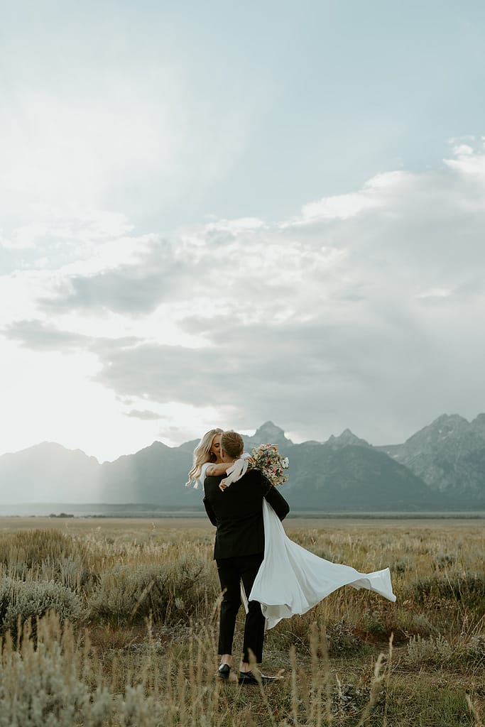 Couple in a vast field with Tetons in the background for their Jackson Hole elopement