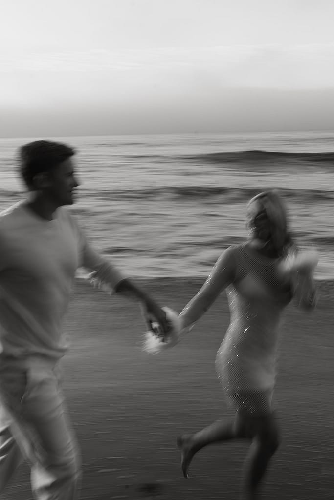 Engaged couple running along the sandy shore of Malibu Beach during sunrise.